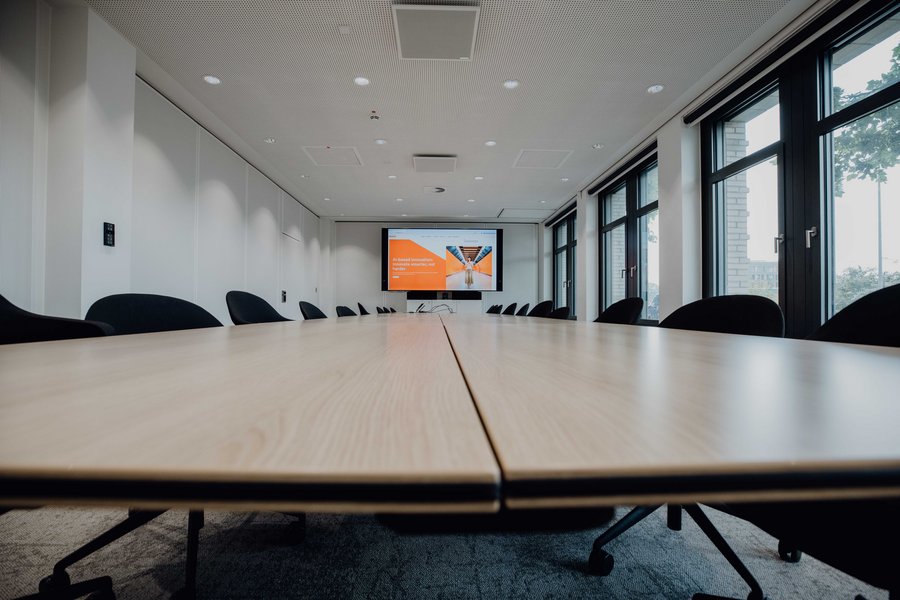 Conference-Room2.jpg Close Up of modern conference room with a long wooden table, black chairs, and a large screen for presentations.